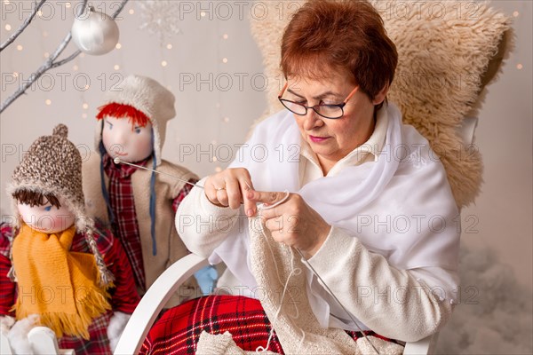A nice elderly woman sews to knit her granddaughters in a Christmas arrangement. In studio
