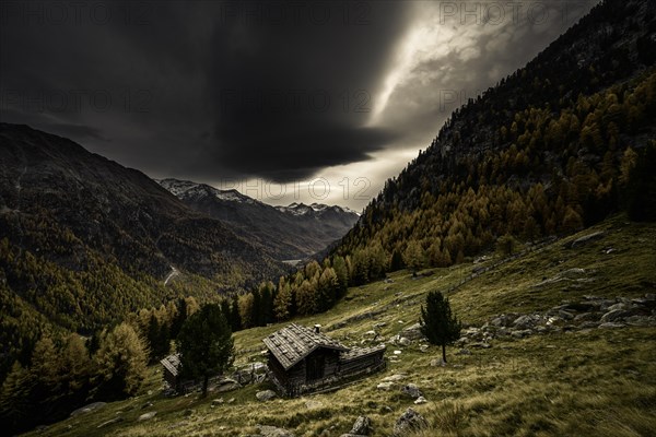 Mountain hut on mountain meadow with autumnal mountain forest and threatening cloudy sky