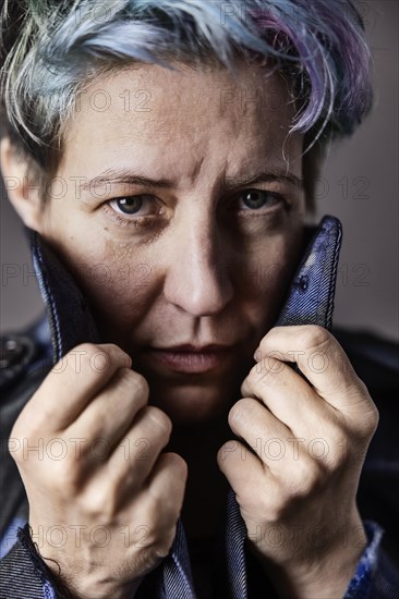 Androgynous woman with dyed hair pulls up the collar of her denim jacket