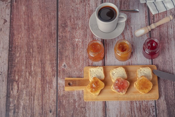 Small pieces of toast with jam and coffee on a wooden table