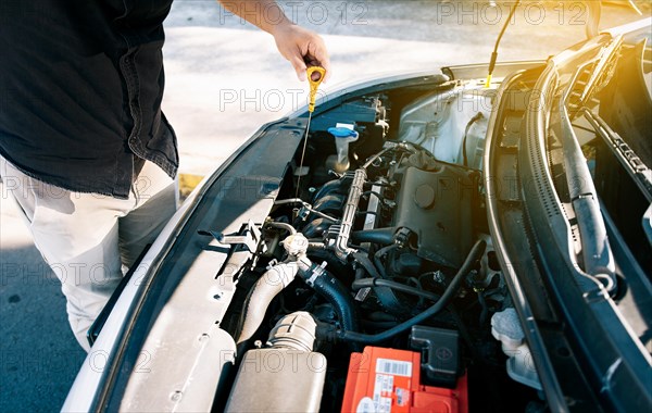 Person checking the oil level of his car in the street. Driver inspecting car oil level