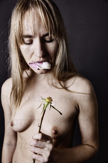 Young naked woman eating the petals of a rose