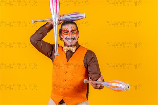 Juggler man in make up vest juggling with maces on a yellow background