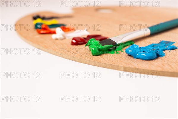 Wooden palette with colored oil paints and brushes isolated on a white background