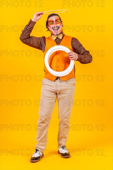 Happy juggler man in makeup vest juggling hoops on a yellow background