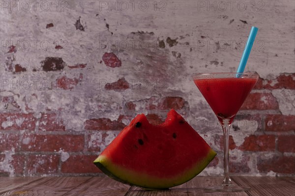 Cocktail glass with watermelon juice and slices of fresh watermelon on a wooden table