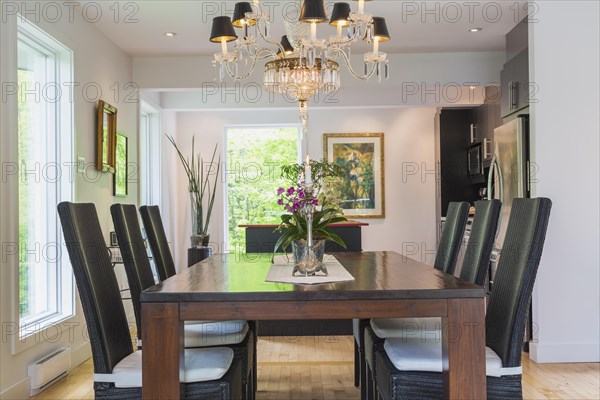 Walnut colored wooden dining table with black high back wicker chairs in dining room inside modern home