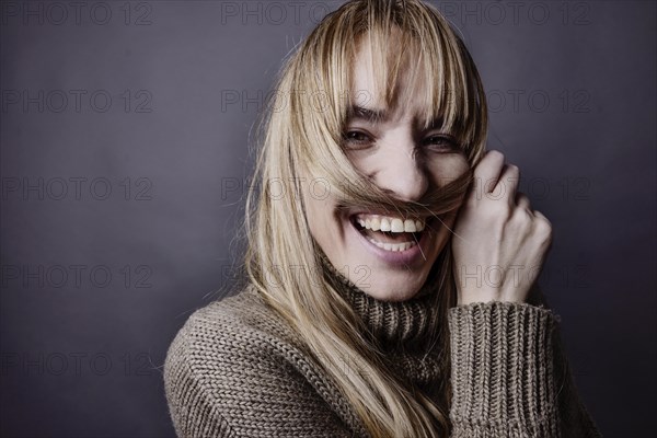 Young woman with long blond hair makes a moustache out of a strand of hair and smiles at camera