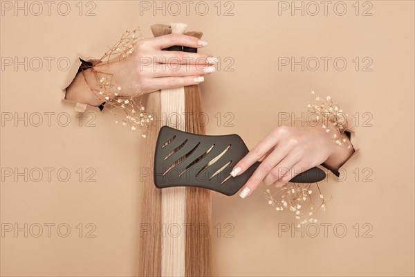 Hands with flowers hold strands of hair for extensions on a beige background. hair beauty