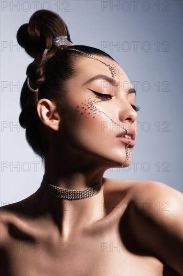 Beautiful woman with creative hairstyle and makeup with rhinestones. Beauty face. Photo taken in the studio