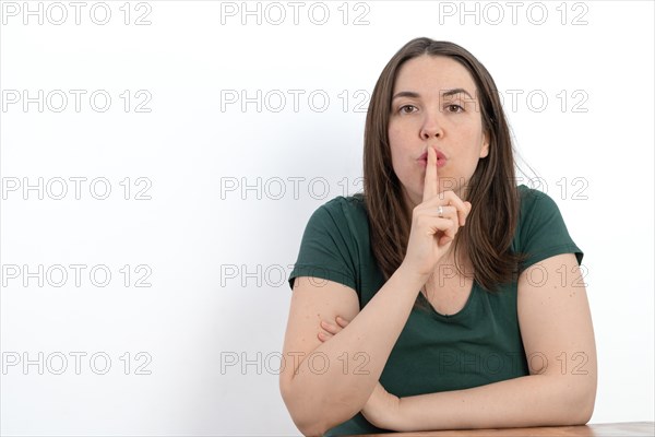 Close-up of young long-haired woman with finger in mouth asking for silence white background
