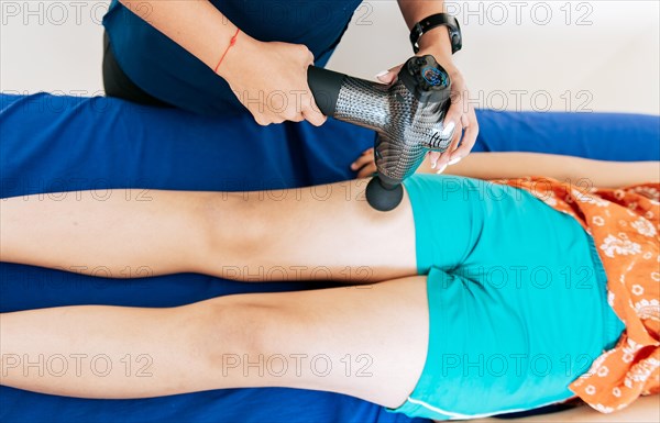 Physiotherapist using massage gun on female patient. Percussion or vibration therapy. Chiropractor using massage gun on patient leg