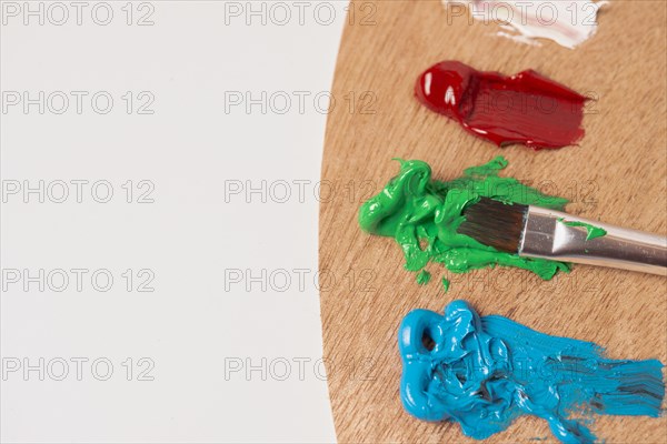 Wooden palette with colored oil paints and brushes isolated on a white background