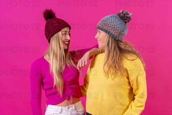 Two blonde caucasian women in wool hats on a pink background