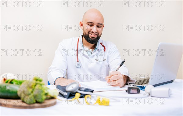Smiling nutritionist writing in the office. Nutritionist writing on notepad. Male nutritionist working with notes and laptop at desk