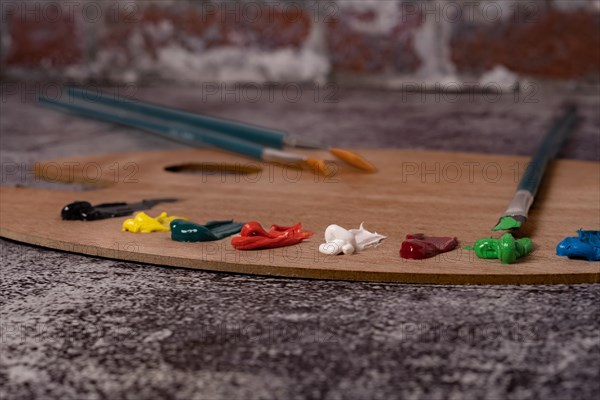 Wooden palette with colored oil paint and brushes with a brick wall in the background