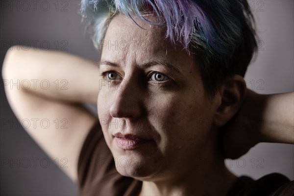 Androgynous woman with dyed hair crosses her arms behind her head