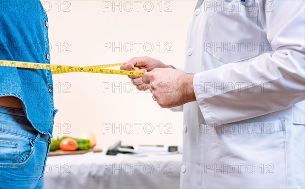 Close up of nutritionist measuring waist to female client. Hands of male nutritionist measuring waist to female patient. Concept of weight loss and professional nutritionist