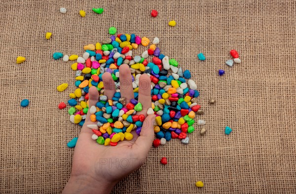 Colorful little pebbles in hand and on canvas ground