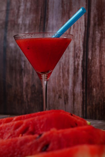 Cocktail glass with watermelon juice and slices of fresh watermelon on a wooden table