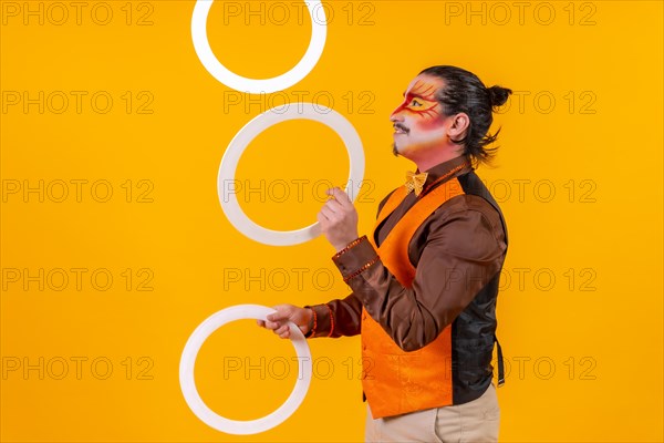 Juggler in a vest and with a painted face juggling hoops on a yellow background