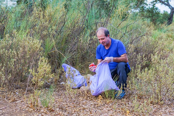 Environmentalist man with garbage bags picking up garbage from the field and taking care of the environment