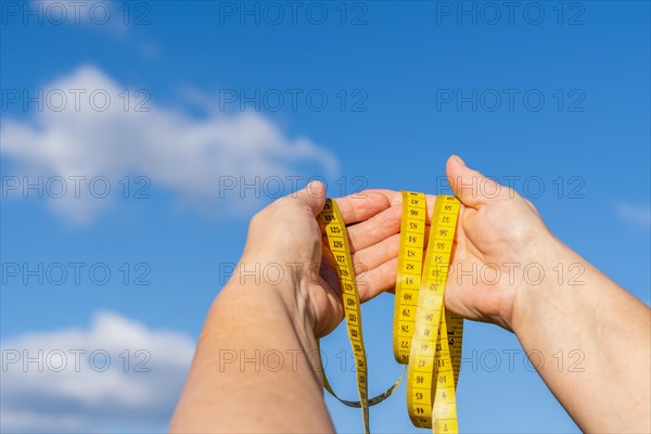 Woman holding in her hands a tape measure with a blue sky and clouds in the background