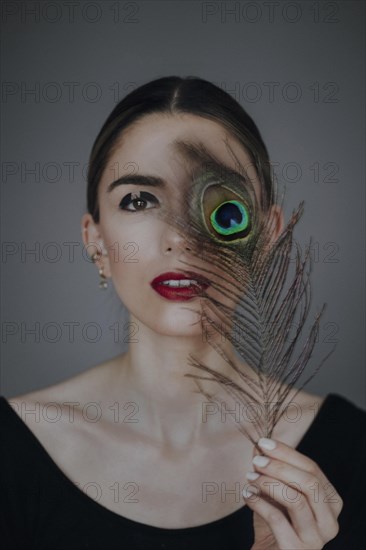 Young woman with peacock feather in front of face
