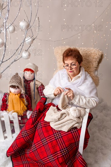 A nice elderly woman sews to knit her granddaughters in a Christmas arrangement. In studio