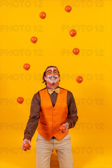 Portrait of a juggler in a vest with a painted face juggling balls on a yellow background