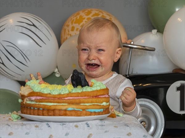 One-year-old boy sits in front of his birthday cake on his first birthday and cries