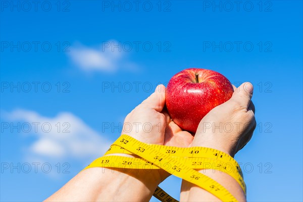 Woman holding an apple in her hands with a tape measure and a sky with clouds in the background