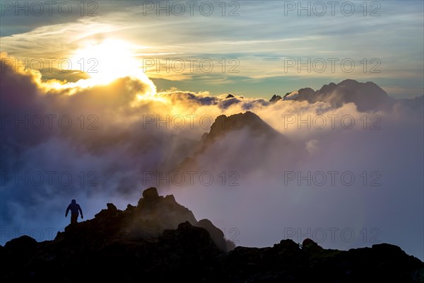 A climber walking along a ridge during a sunrise in the clouds