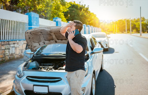 Frustrated man with damaged car calling technician on the road. Young man with damaged car calling the mechanic. Driver with the damaged car calling the mechanic