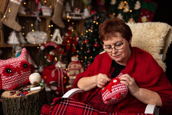 Grandmother sews a plush owl in Christmas arrangement. In studio