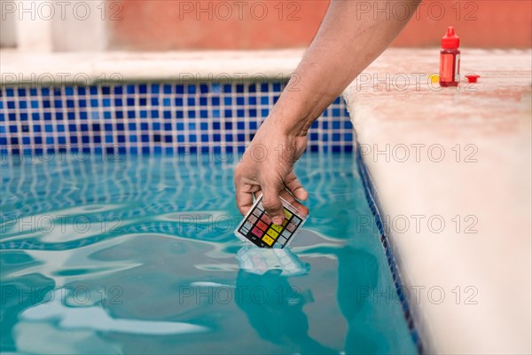 Close up of person testing the ph of the water with mini tester in swimming pool. Hand testing pool water for chlorine with PH mini tester. Testing the chlorine and PH of swimming pool