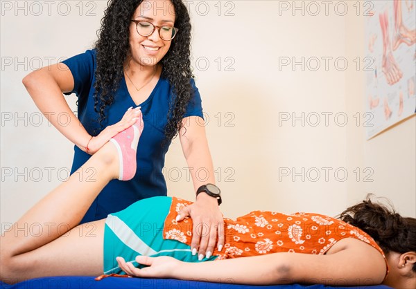 Physiotherapist woman assisting knee to lying patient. Knee flexion physiotherapy to female patient