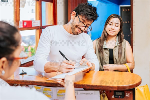 Couple signing in at a hotel reception. Young couple signing documents in a hotel reception. Latin couple signing reservation at hotel reception. Hotel reservation concept