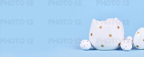 Banner with white easter eggs with golden dots and egg cup on blue background with copy space