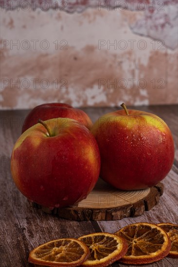 Close-up of three fresh red apples with drops of water on a slice of wood