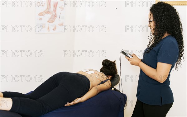 Physiotherapist electrostimulating a patient. Lower back therapy with electrode pads. Electrode treatment to patient lying down