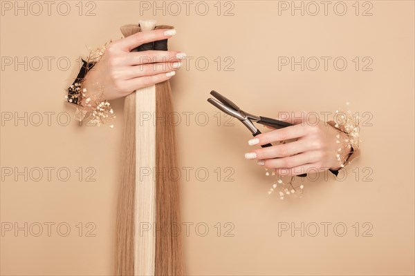 Hands with flowers hold strands of hair for extensions on a beige background. hair beauty