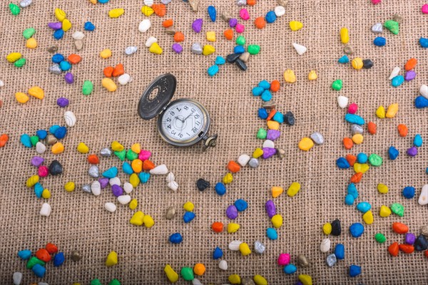 Pocket watch amid colorful pebbles on canvas background