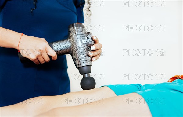 Physiotherapist using massage gun on female patient. Physiotherapist hand using massage gun on patient. Chiropractor using massage gun on patient leg with copy space