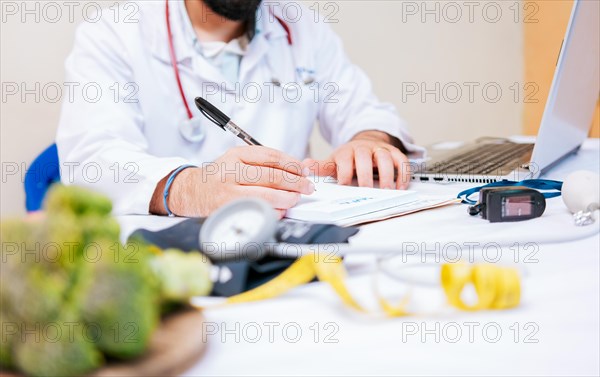 Close-up of nutritionist writing on notepad. Hands of male nutritionist taking notes at his desk