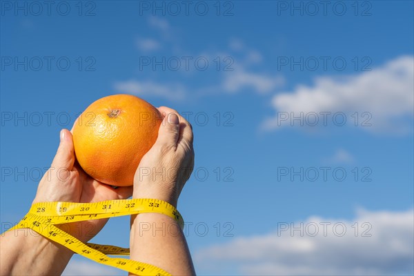 Woman holding a grapefruit in her hands with a tape measure and a sky with clouds in the background