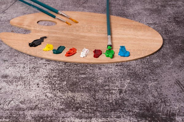 Wooden palette with colored oil paint and brushes with a brick wall in the background