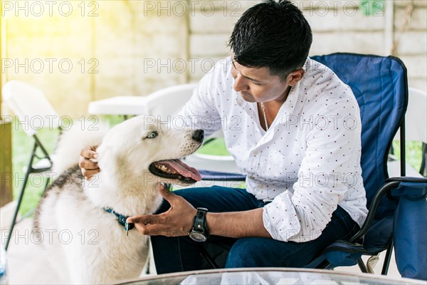 Guy sitting playing with his husky dog. Young man sitting petting his dog in the backyard. Concept of person petting his husky dog