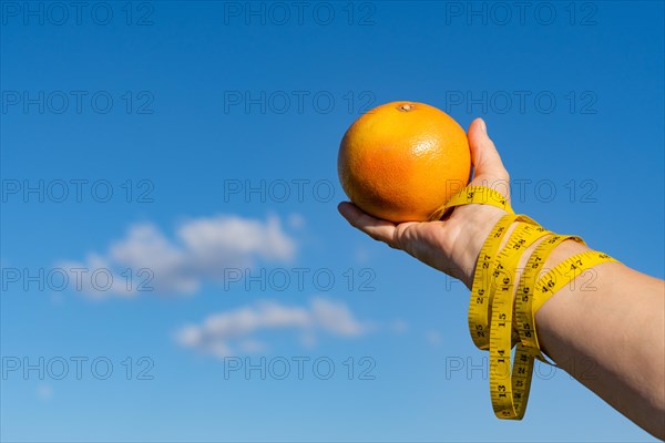 Woman holding a grapefruit in her hands with a tape measure and a sky with clouds in the background