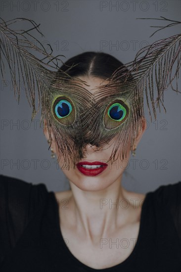 Young woman with peacock feather in front of face